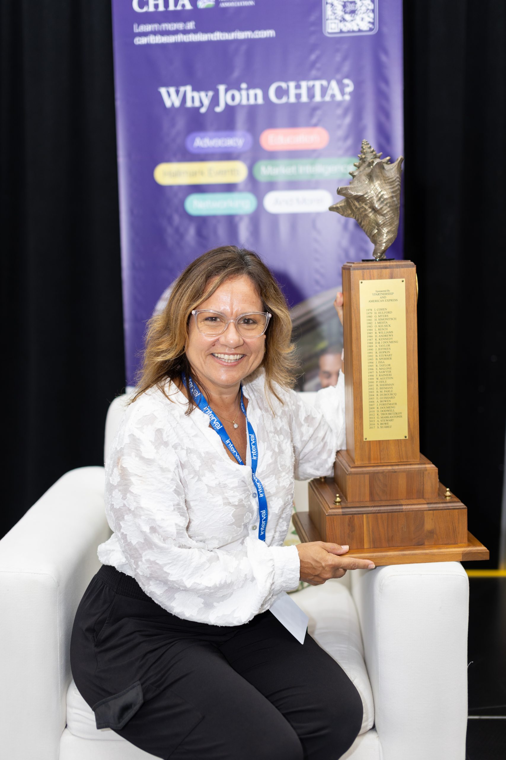 Patricia Affonso-Dass, CHTA 2024 Hotelier of the Year posing on a white chair with a trophy.